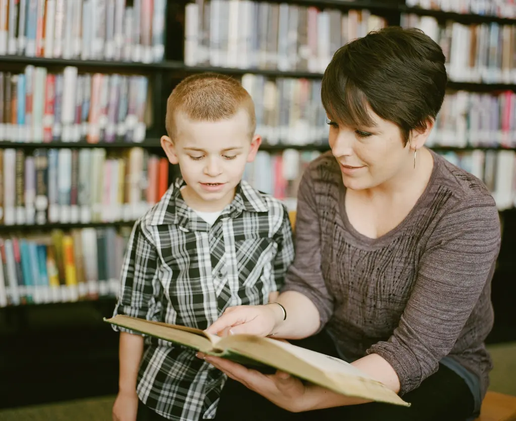 A woman and a boy reading a book together in a library