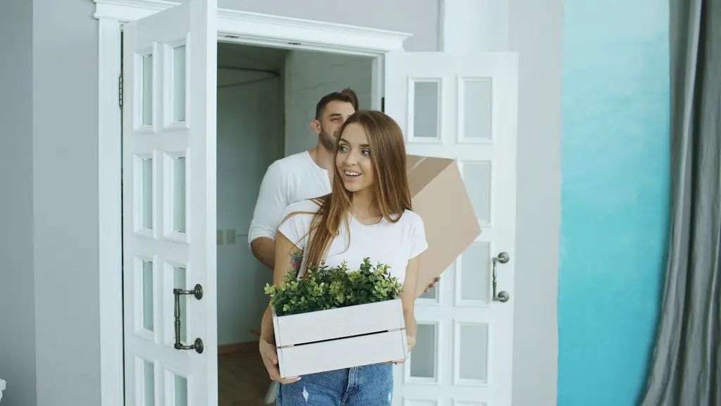 A couple carrying boxes and a plant into a new home