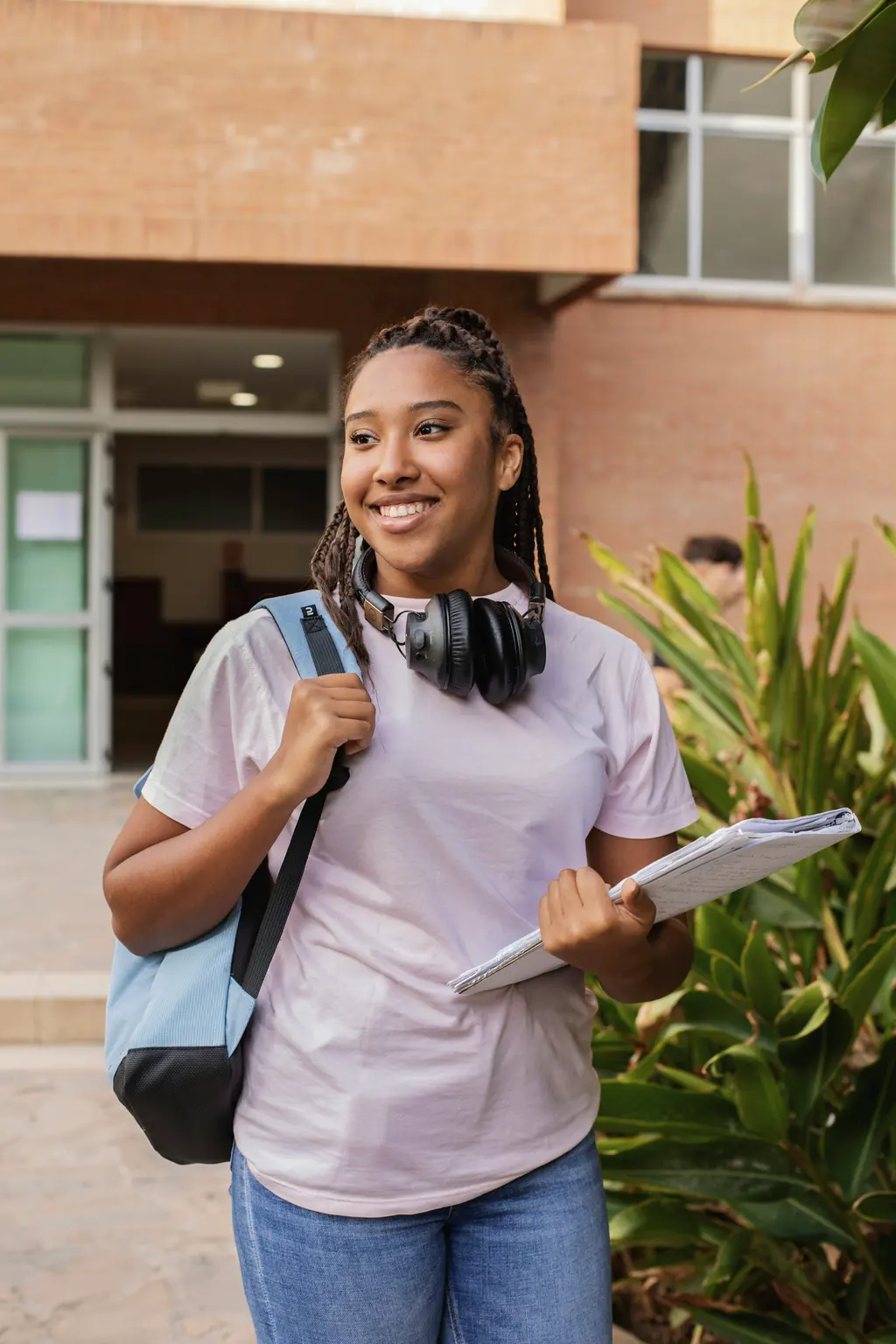 A smiling student with a backpack and books walking outside